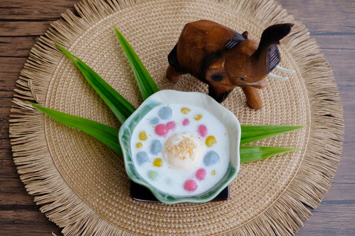 Bua Loy (บัวลอย)  ist ein buntes Allerlei aus gefärbten Reisbällchen in warmer Kokosmilch und hier auf dem Bild mit einem Ei serviert. Ein Holzelefant als Dekoelement runden das Bild ab.