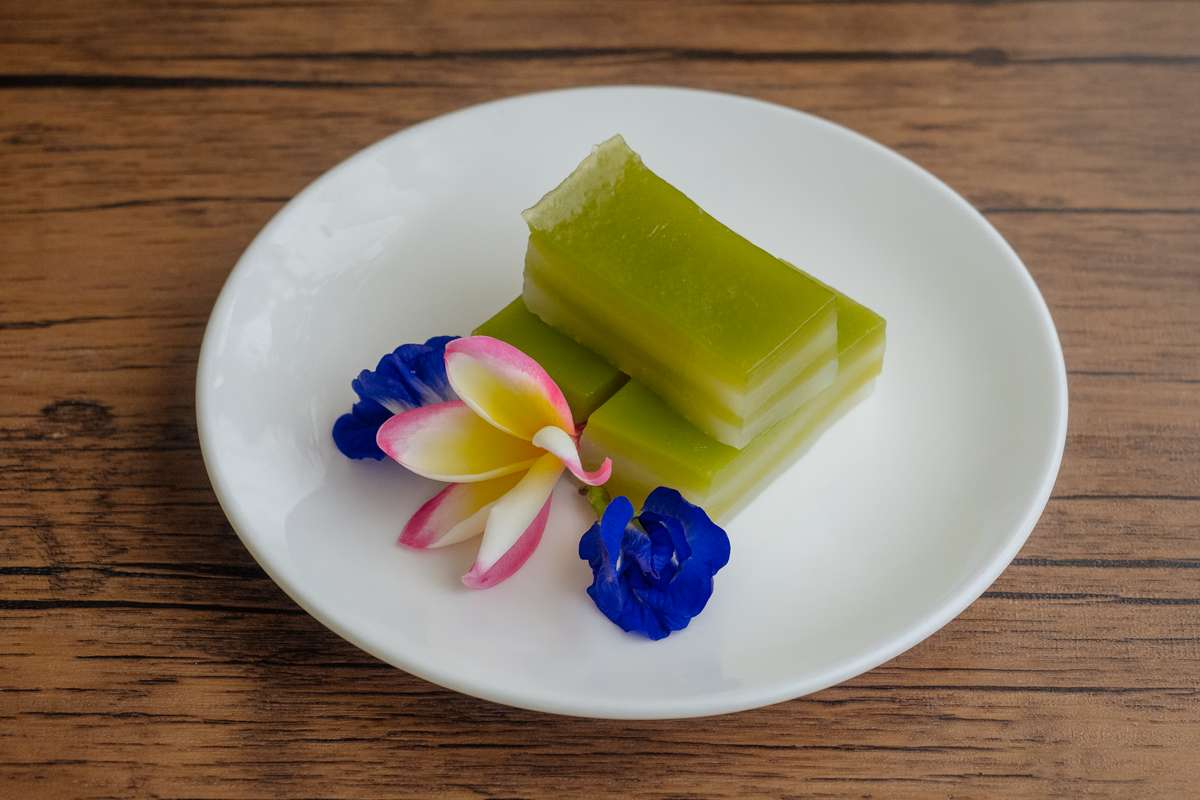 Das geschichtete Dessert Khanom Chan (ขนมชั้น) mit tropischen Blumen dekoriert.