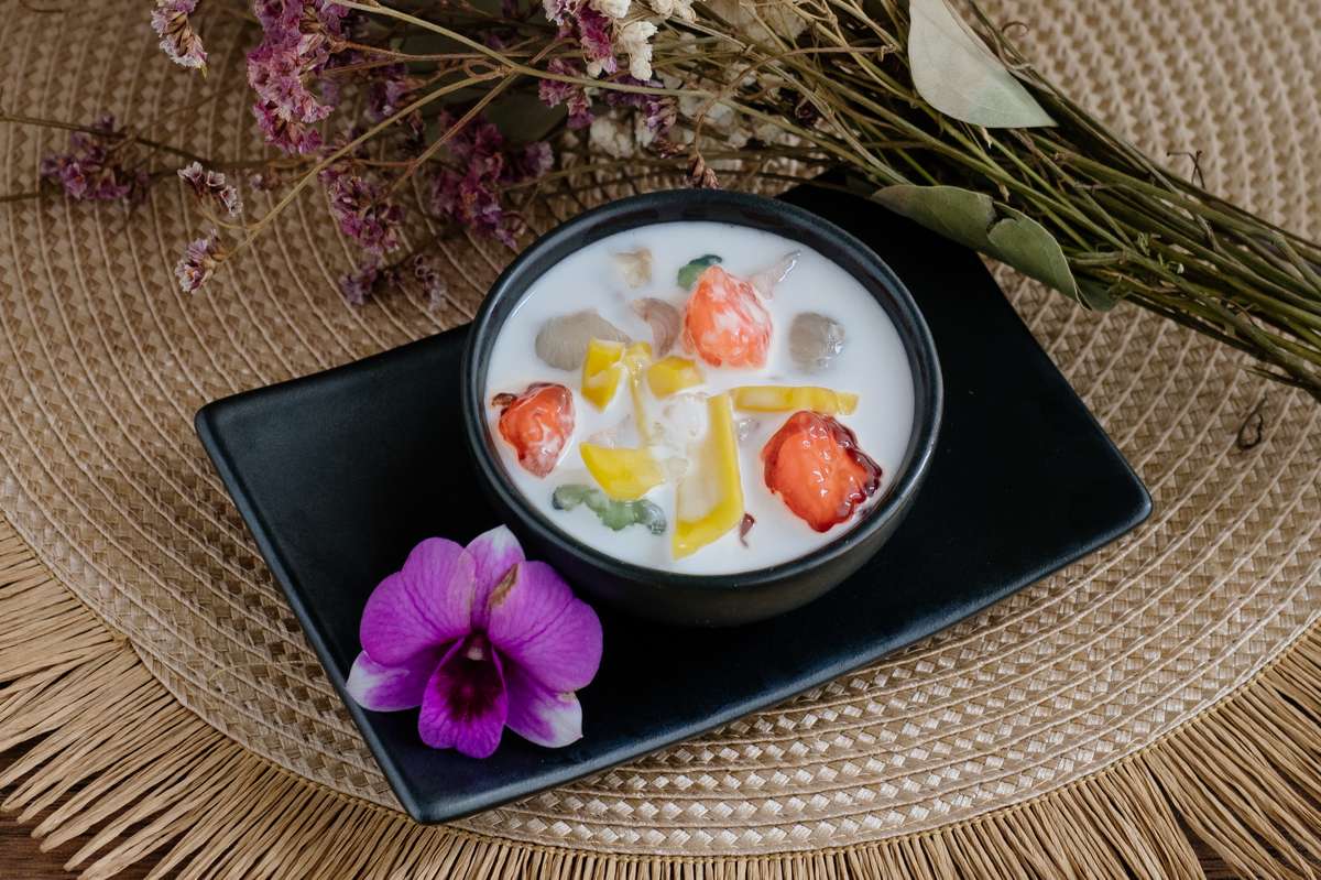 Die erfrischende thailändische Nachspeise Tub Tim Grob (ทับทิมกรอบ) liebevoll in einer schwarzen Schale angerichtet. Eine kleine Lotusblüte ziert das Arrangement