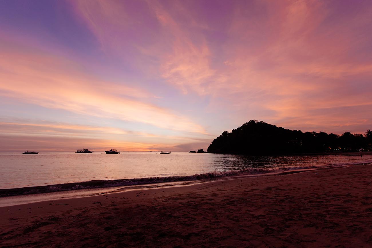 Der Himmel über Koh Lanta erstrahlt in der Himmel in leuchtenden Orange-, Pink- und Lilatönen.