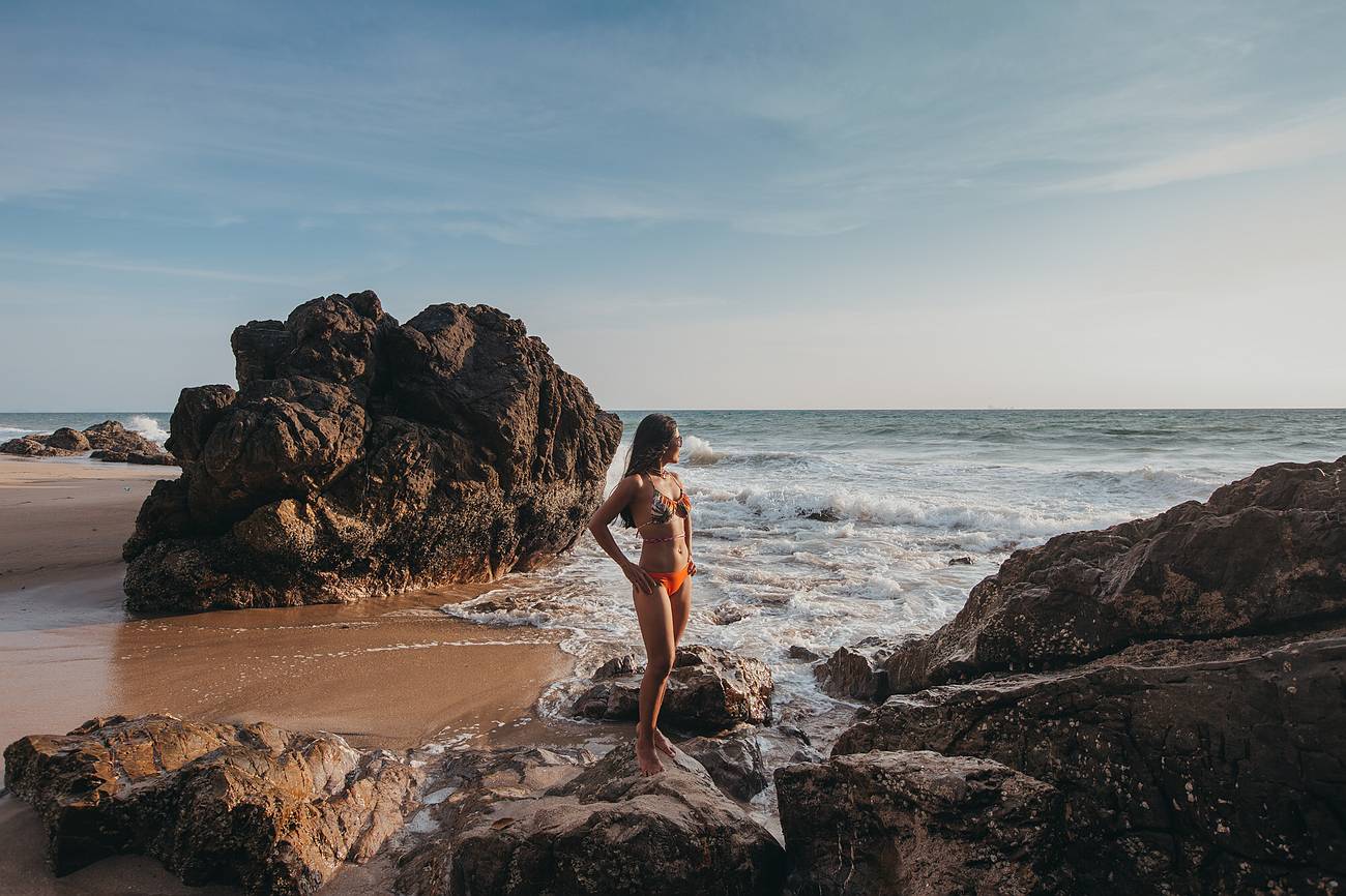 Channa steht auf Felsen am Strand von Koh Lanta bei leichtem Wellengang – typisches Wetter in der Übergangszeit zur Regenzeit mit wechselhaften Bedingungen